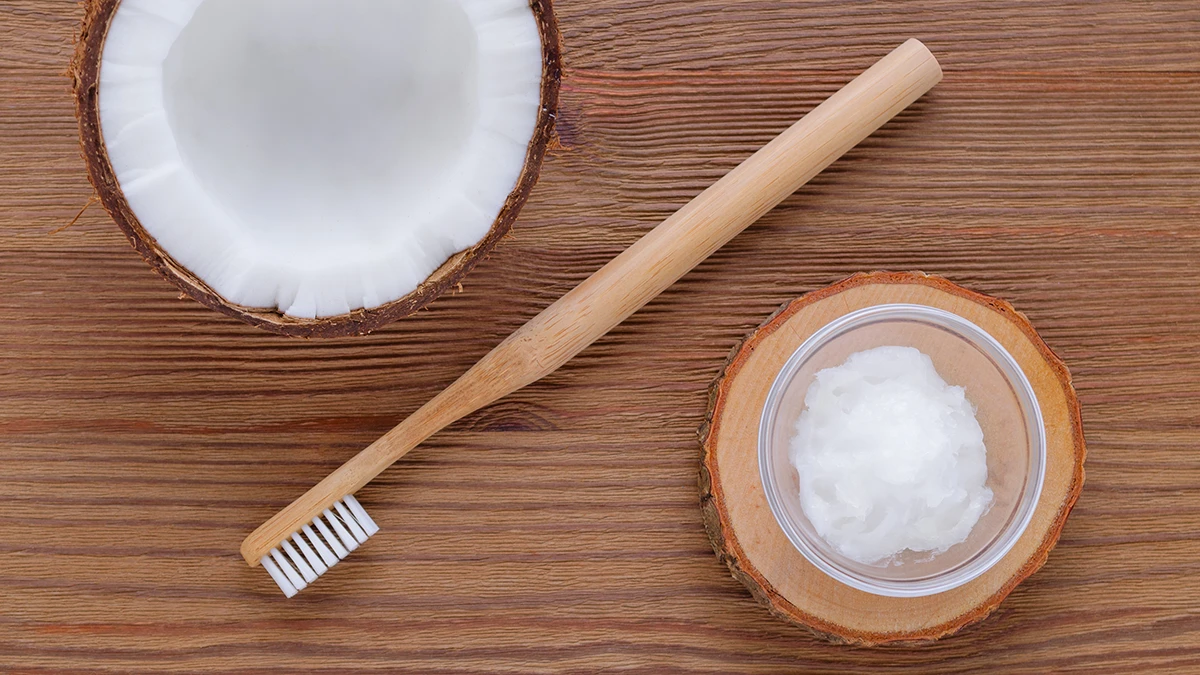 Coconut oil, half a coconut, and a toothbrush on a wooden table